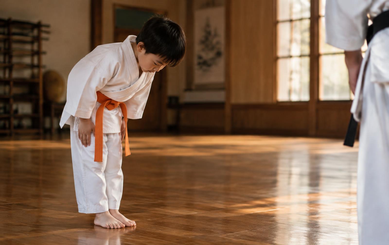 Young karate student in a white gi and orange belt bowing in a traditional dojo